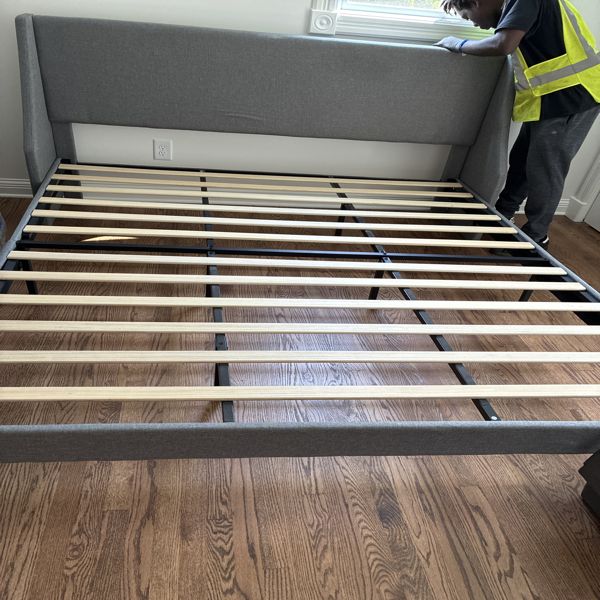 Crew member in a high-visibility vest assembling a bed frame after delivery